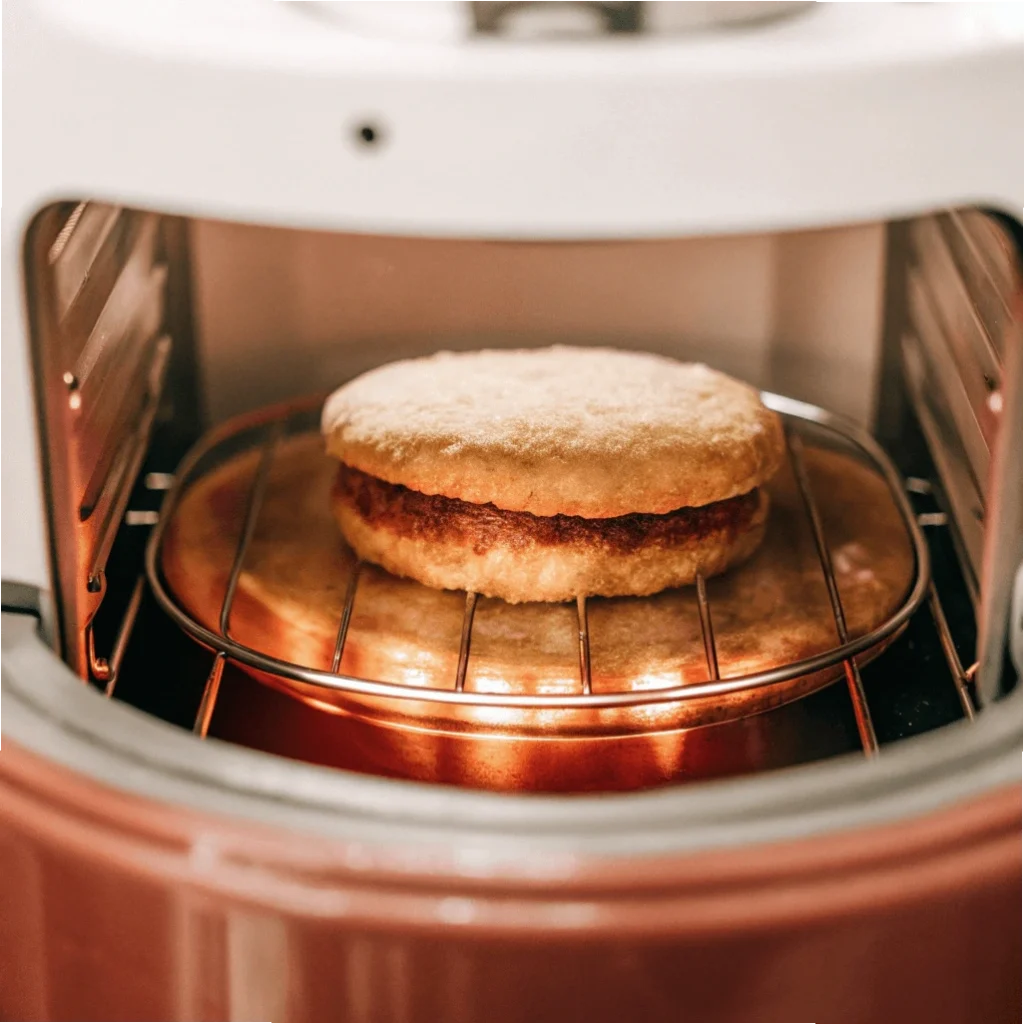 A frozen breakfast sandwich cooking in an air fryer on a wire rack.