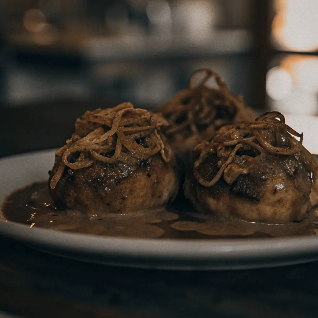 A close-up of smothered potatoes served on a plate, topped with crispy onions and a rich sauce.